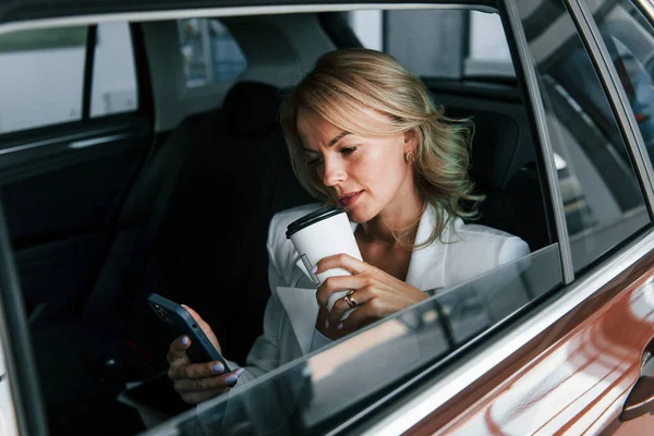 Side view. Woman in formal clothes is indoors in the autosalon.