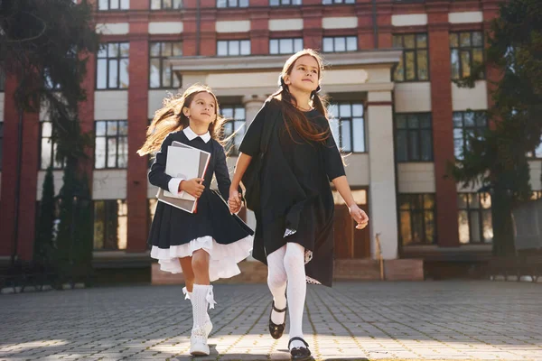 2人の女子学生が校舎の近くで一緒に外に走っています — ストック写真