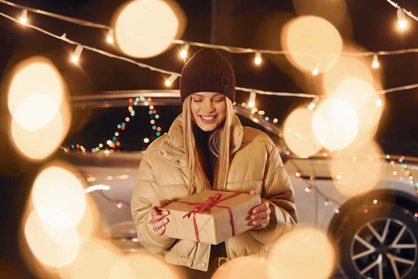 Holding gift box. Woman standing in the forest and celebrating New year.