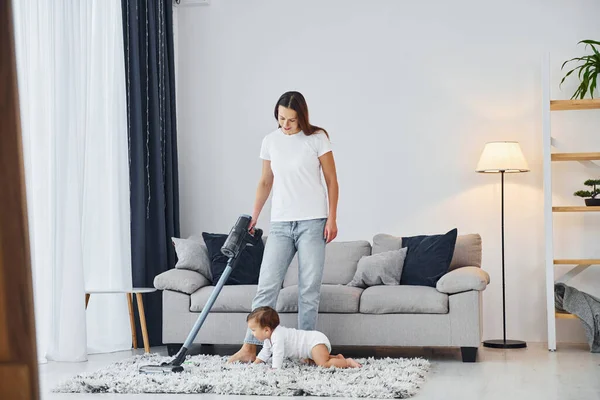 掃除機を使って床を掃除する 母親と娘は屋内で一緒に家にいる — ストック写真