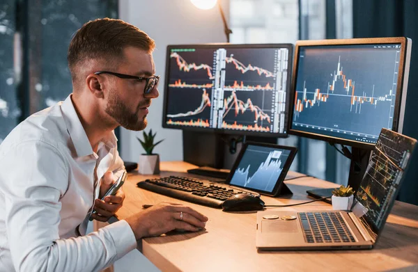 Akşamları çalışıyorum. Resmi giyinmiş genç işadamı birden fazla ekranla ofiste..