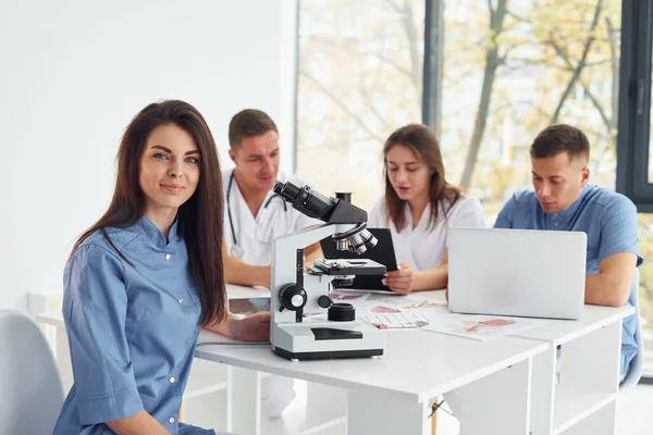 顕微鏡を使う 若い医師のグループが現代のオフィスで一緒に働いています — ストック写真