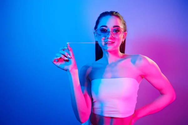 Positive emotions. Fashionable young woman standing in the studio with neon light.