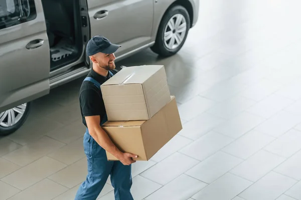 Business of service. Delivery man in uniform is indoors with car and with order.