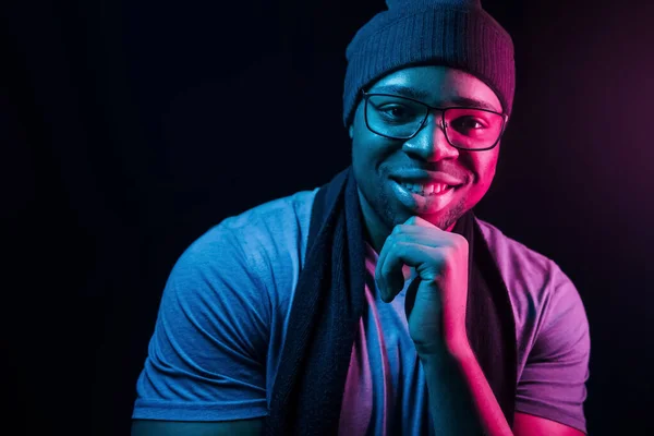 In hat and scarf. Futuristic neon lighting. Young african american man in the studio.