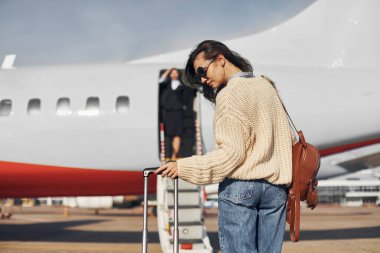 At daytime. Young female passanger in casual clothes is outdoors near the plane. clipart