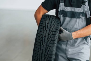 Üniformalı adam gündüz vakti otomatik kanalda çalışıyor. Lastiği ellerinde tutarak.
