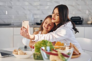 Mutfakta. Beyaz tenli genç bir anne kızıyla birlikte evde..