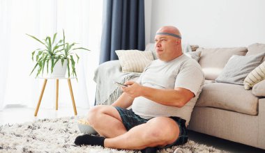 Kanepede patlamış mısırla oturuyor. Sıradan giysili komik şişman adam evde..