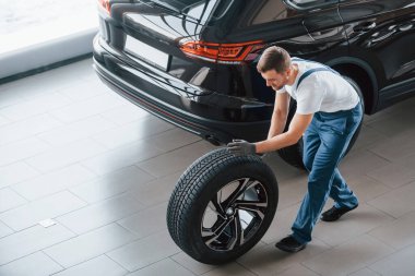Tekerlek değiştirme. Beyaz gömlekli ve mavi üniformalı genç adam otomobil tamir ediyor..