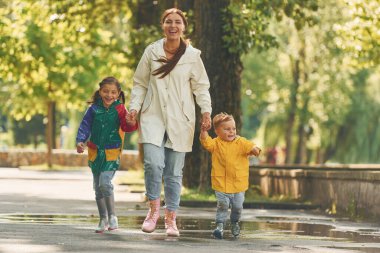 Ön manzara. Anne, küçük oğlu ve kızıyla yağmurdan sonra parkta yürüyüşe çıktı..