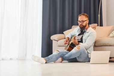 Yaratıcı uğraş. Gündelik giysiler içinde ve akustik gitarlı bir adam içeride..