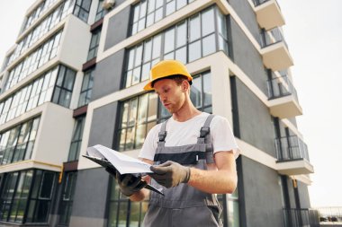 Modern şehir. Gündüz vakti inşaatta üniformalı genç bir adam çalışıyor..