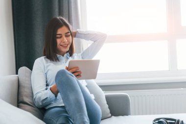 Elinde dijital tabletle. Genç kadın, gündüz vakti modern evin içinde..