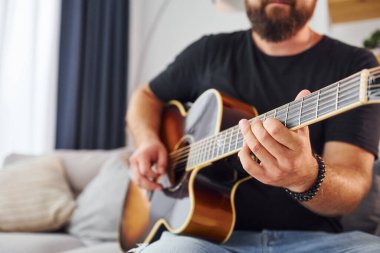 Enstrüman çalıyorum. Gündelik giysiler içinde ve akustik gitarlı bir adam içeride..