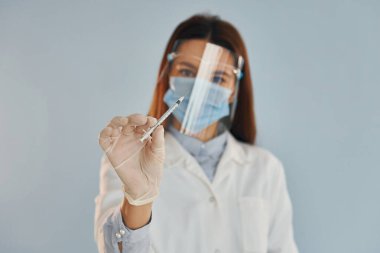 Şırınga tutuyor. Beyaz önlüklü genç bayan doktor içeride duruyor..