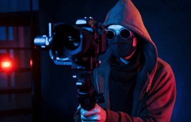 Kapüşonlu, kameralı adam. Neon ışıkları. Genç Avrupalı adam karanlık stüdyoda..