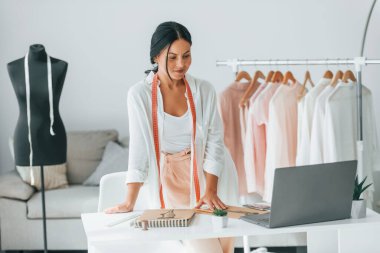 Dizüstü bilgisayarla. Terzi odasında, farklı kıyafetlerle..