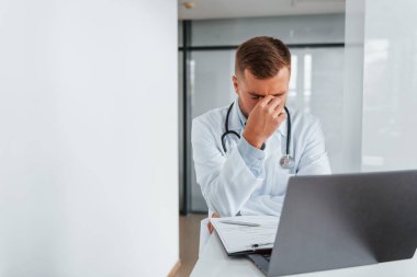 Dizüstü bilgisayar kullanmak ve yorgun hissetmek. Klinikte beyaz önlüklü profesyonel doktor var..