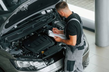 Motor tamiri. Üniformalı adam gündüz vakti otosalonda çalışıyor..