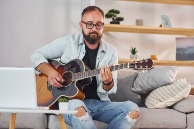 Şarkı yazma süreci. Gündelik giysiler içinde ve akustik gitarlı bir adam içeride..