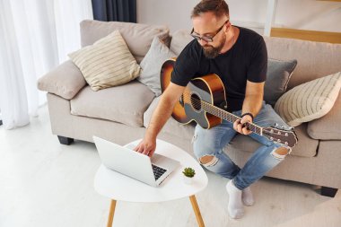 Laptop kullanıyorum. Gündelik giysiler içinde ve akustik gitarlı bir adam içeride..