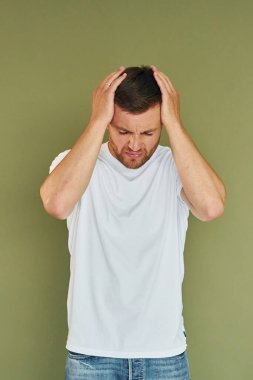 Stüdyoda günlük giysiler içinde duran genç bir adam. Beyaz gömlekli..