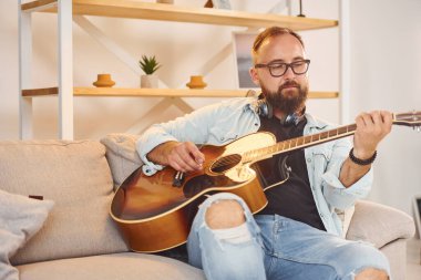 Yaratıcı uğraş. Gündelik giysiler içinde ve akustik gitarlı bir adam içeride..