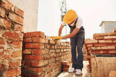 Tuğla kullanarak. Üniformalı genç inşaat işçisi tamamlanmamış binada meşgul..