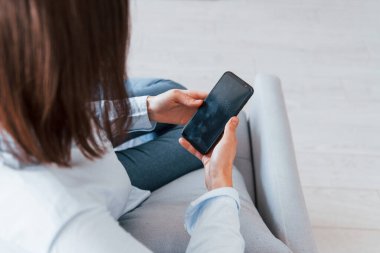 Akıllı telefonunla oturuyor. Genç kadın, gündüz vakti modern evin içinde..
