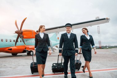 Bagajlı. İş üniformalı uçak mürettebatı uçağın yanında birlikte..