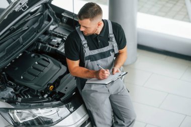 Motor tamiri. Üniformalı adam gündüz vakti otosalonda çalışıyor..