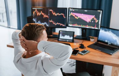 Dinleniyorum. Resmi giyinmiş genç işadamı birden fazla ekranla ofiste..