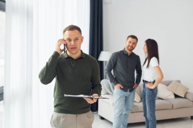 Satıcı, genç bir çiftin daire seçmesine yardım ediyor. İş ve kira kavramı.