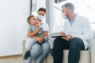 İncelenen küçük çocukla. Beyaz önlüklü iki doktor klinikte birlikte çalışıyorlar..