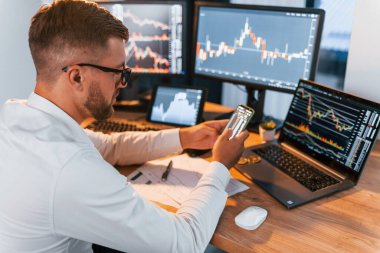 Yan görüş. Resmi giyinmiş genç işadamı birden fazla ekranla ofiste..