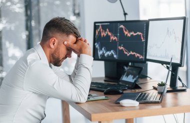 Riskli bir iş. Resmi giyinmiş genç işadamı birden fazla ekranla ofiste..