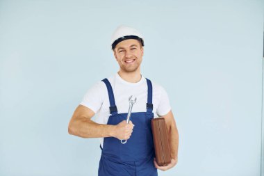 Kahverengi çantayı tutuyorum. Üniformalı ve kasklı bir işçi stüdyoda ekipmanla bekliyor..