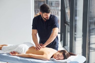 Oda güneş ışınlarıyla aydınlatılıyor. Genç bir kadın, erkek kaplıcada vücuduna masaj yaparken uzanır..