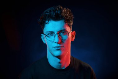 Siyah arka plana karşı. Neon ışıkları. Genç Avrupalı adam karanlık stüdyoda..