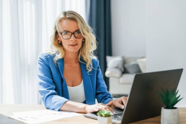 Dizüstü bilgisayarla birlikte masada oturuyor. Gündelik elbiseli kadın evde..