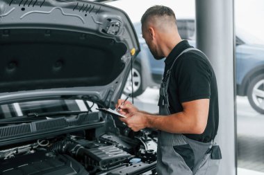 Kaputun altında. Üniformalı adam gündüz vakti otosalonda çalışıyor..