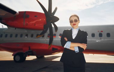 Resmi siyah elbiseli genç hostes uçağın yanında dikiliyor..