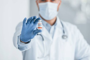 COVID-19 aşısıyla test tüpünü tutuyorum. Klinikte beyaz önlüklü profesyonel doktor var..