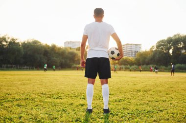 Ayakta duruyor ve topu elinde tutuyor. Genç futbolcu spor sahasında antrenman yapıyor..