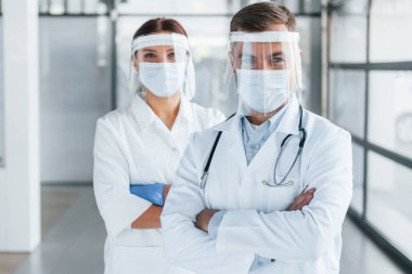 Kollarını kavuşturmuş duruyorsun. Beyaz önlüklü iki doktor klinikte birlikte çalışıyorlar..