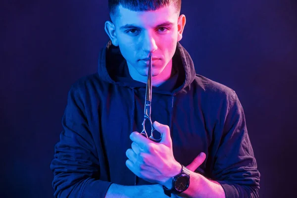 Trzyma Nożyczki Młody Fryzjer Sprzętem Roboczym Stojący Studio Oświetleniem Neonowym — Zdjęcie stockowe