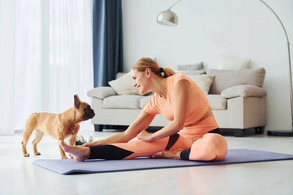 Woman in yoga clothes with pug dog is at home at daytime.