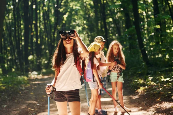 女孩站在她的朋友面前 孩子们带着旅行器材在森林里散步 — 图库照片