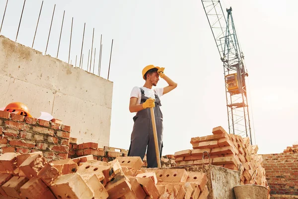 Tired man. Young construction worker in uniform is busy at the unfinished building.